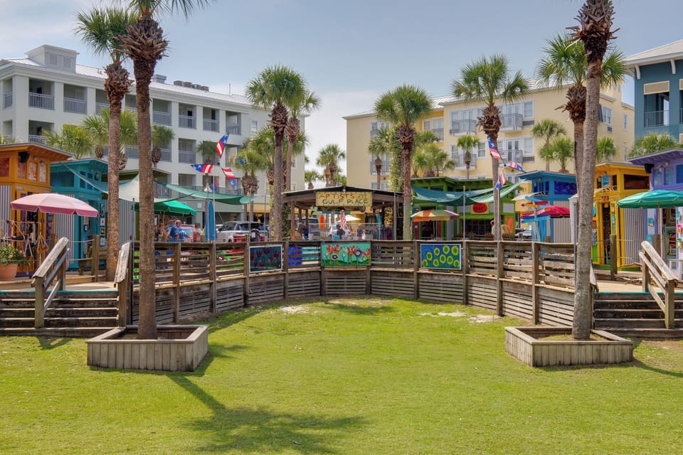 Colorful beachfront playground with slides and climbing structures surrounded by palm trees and modern resort buildings.
