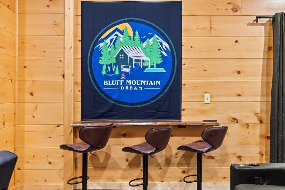 Rustic wooden wall with a mounted bar counter and three leather stools under a bluff mountain dream tapestry.