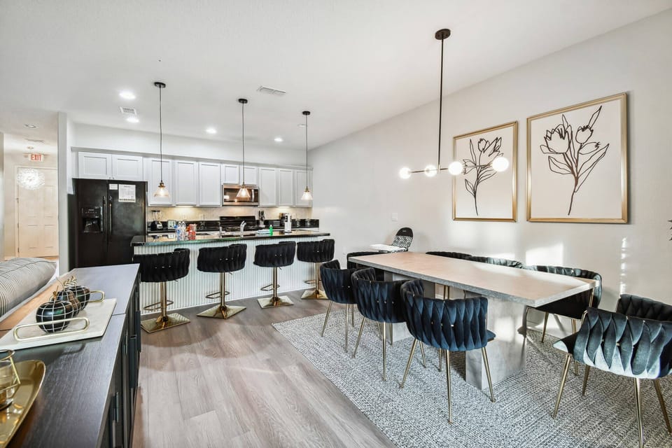 Begin your mornings in this chic open kitchen and dining area, featuring sleek black bar stools and a modern table with cozy chairs. The elegant decor and warm lighting create an inviting atmosphere for meals and gatherings.