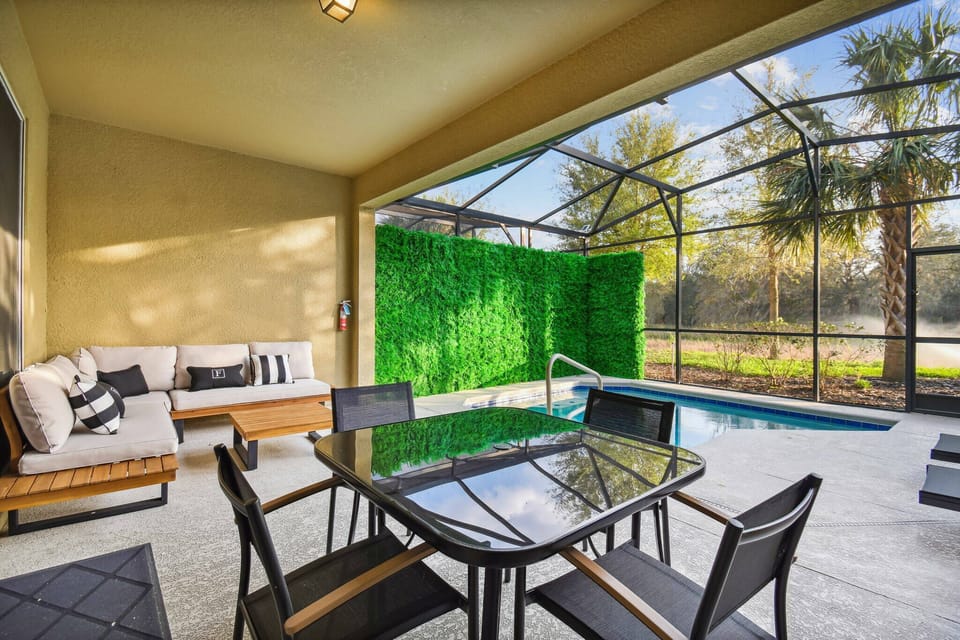 Discover a chic outdoor lounge with sleek black furniture against a vibrant green wall, offering a refreshing atmosphere. Unwind by the sparkling pool, embraced by nature for a perfect escape from daily life.