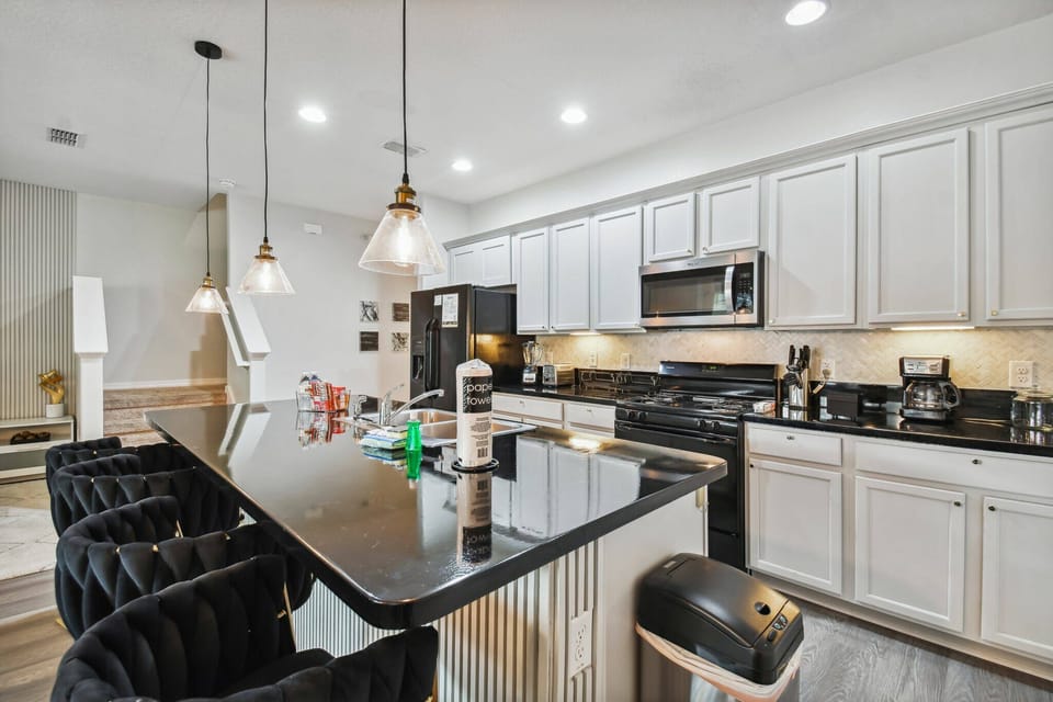 Experience a stylish kitchen with sleek black countertops and white cabinetry, ideal for your culinary creations. The modern pendant lights above the inviting bar seating create a warm ambiance for morning coffee or evening.