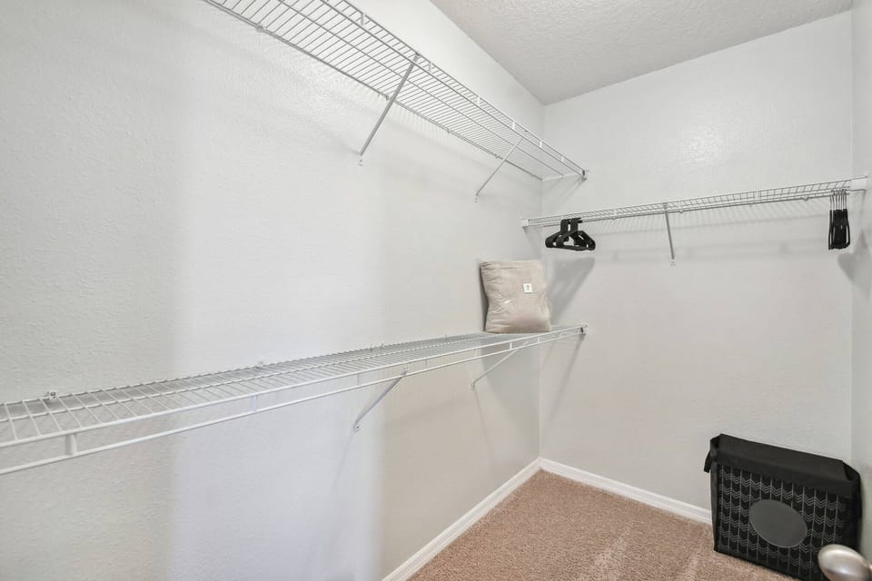 This spacious walk-in closet offers a practical wire shelving system for ample storage. With neutral-toned walls and plush carpeting, it creates a comfortable space to organize and relax during your visit.