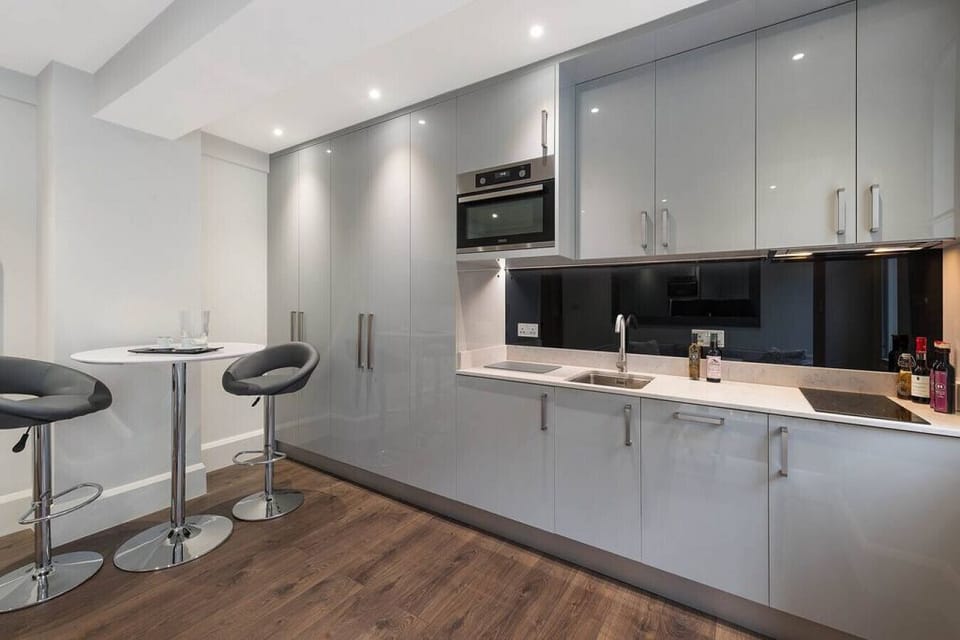 Kitchen — fully equipped straight-run kitchen with marble worksurfaces, bespoke cabinetry, and hardwood flooring. Hob, oven, microwave, fridge-freezer, dishwasher, washer/dryer, coffee machine, kettle, toaster, and cooking utensils