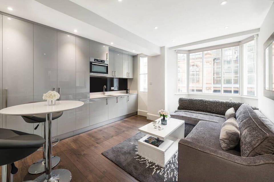 Living room — open-plan space with hardwood flooring, bespoke cabinetry, blackout blinds, ceiling lights and lamp, wall mirror, and bar table with stools. Large Smart TV with Netflix and Amazon Prime. Double sofa bed always made up and ready to use