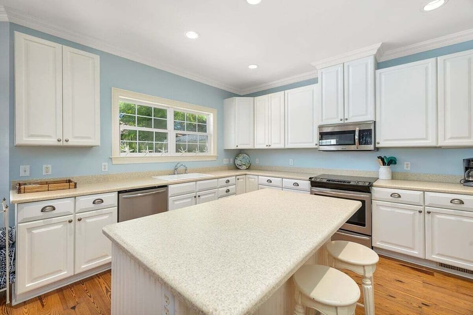 White kitchen with island, stainless appliances, and window