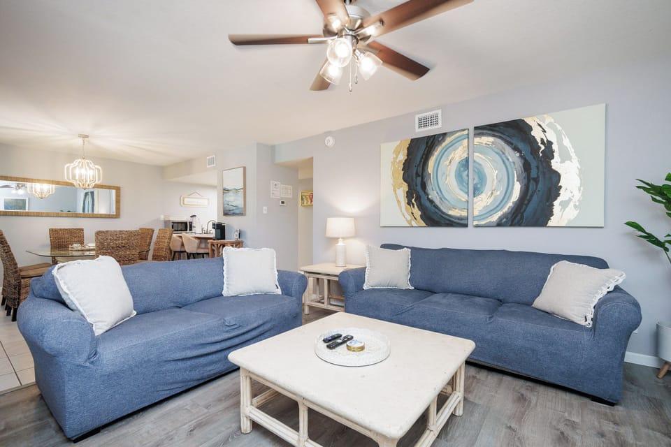Unwind in your coastal-inspired living space with comfortable blue sofas, abstract ocean artwork, and an open layout perfect for relaxing.