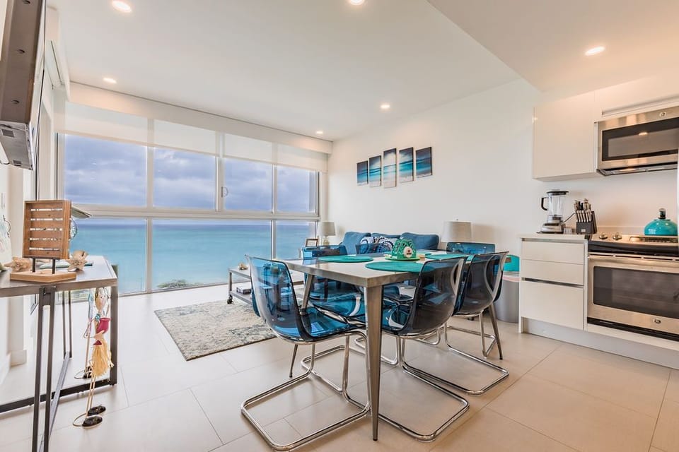 Modern open-concept space where coastal blues meet comfort. Floor-to-ceiling windows frame stunning turquoise waters, while thoughtfully curated décor echoes the sea's palette. Your culinary adventures await in a fully equipped kitchen.