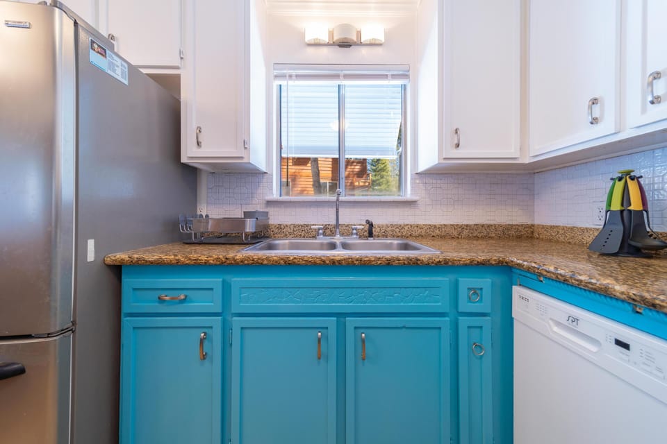 Kitchen sink area with granite countertops, turquoise lower cabinets, white upper cabinets, and stainless steel fridge.