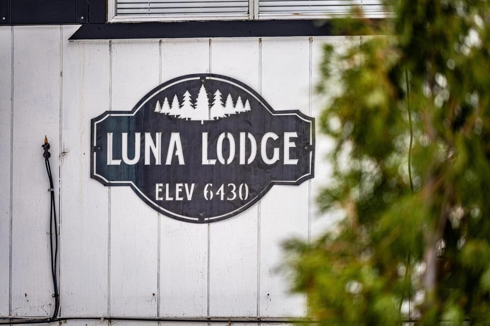 Metal sign with tree silhouettes and elevation detail mounted on white vertical wood siding.