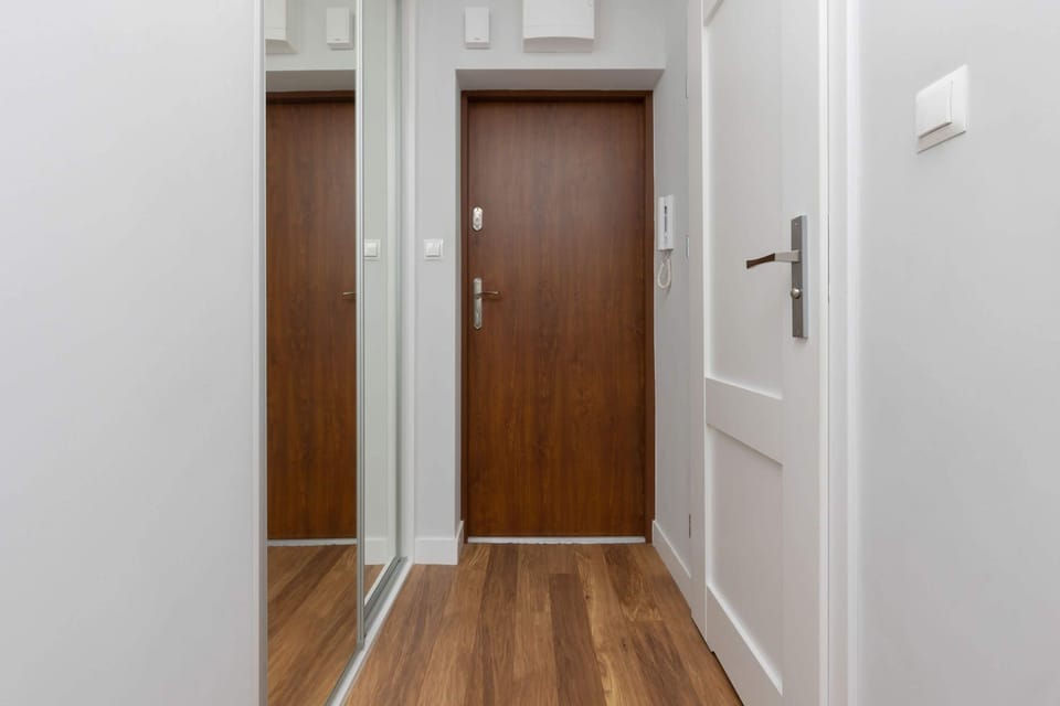 A hallway with wooden floors and white walls, leading to a doorway. The minimalist, clean design suggests it could be the entrance to an apartment or home.