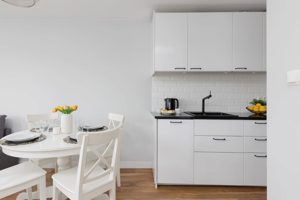 A minimalist dining area with a round white table and two chairs. The table is set for a meal, and a large window brings in plenty of natural light.
