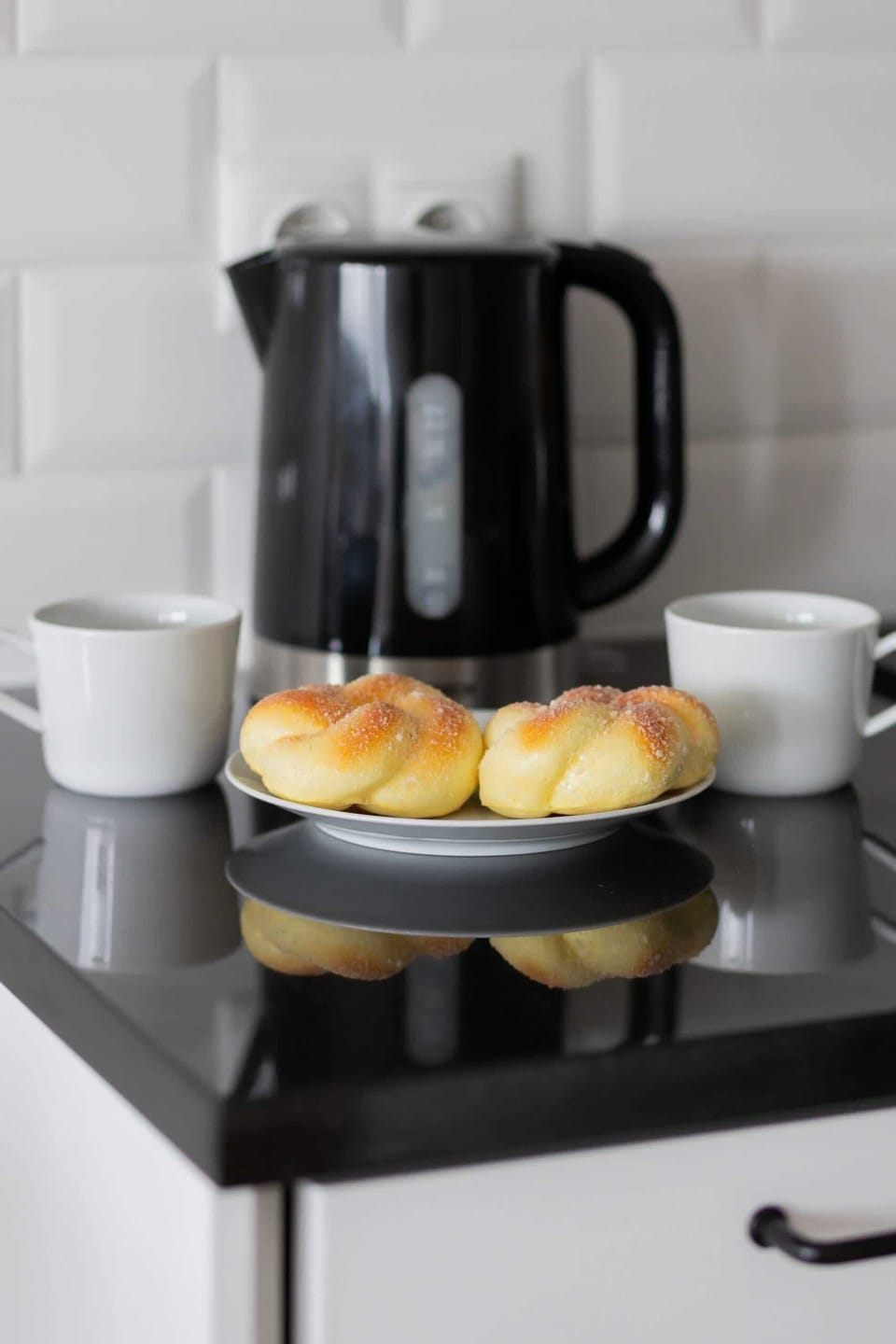 A close-up of an electric kettle on a countertop with two cups and biscuits next to it. The set-up is inviting, suggesting a cosy coffee break.