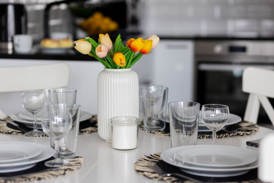 A minimalist dining area with a round white table and two chairs. The table is set for a meal, and a large window brings in plenty of natural light.