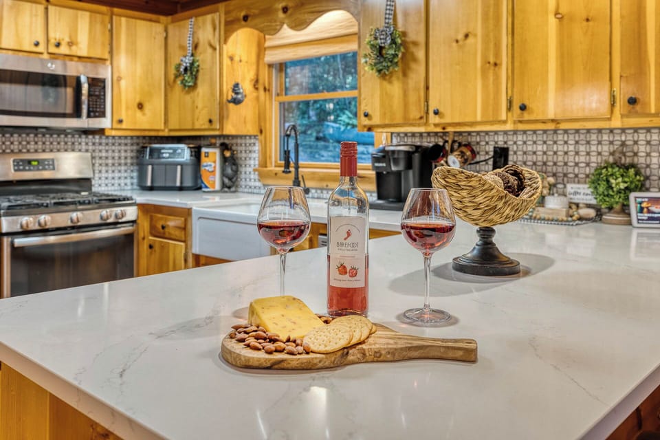 An open kitchen with a large island and ample counter space overlooks the dining area, living room, and a cozy stone fireplace. It features a bar with seating, ideal for gatherings and entertaining.