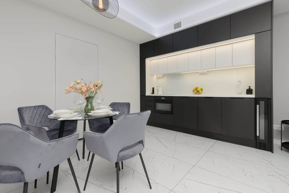 A minimalist kitchen with white cabinets and black countertops, featuring modern appliances, and a large window that allows natural light to brighten the space.