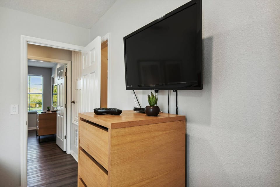 This cozy bedroom, with a sleek wooden dresser and a flat-screen TV, offers a stylish atmosphere. The warm furniture tones and soft natural light from the nearby doorway create an inviting ambiance for a relaxing stay.