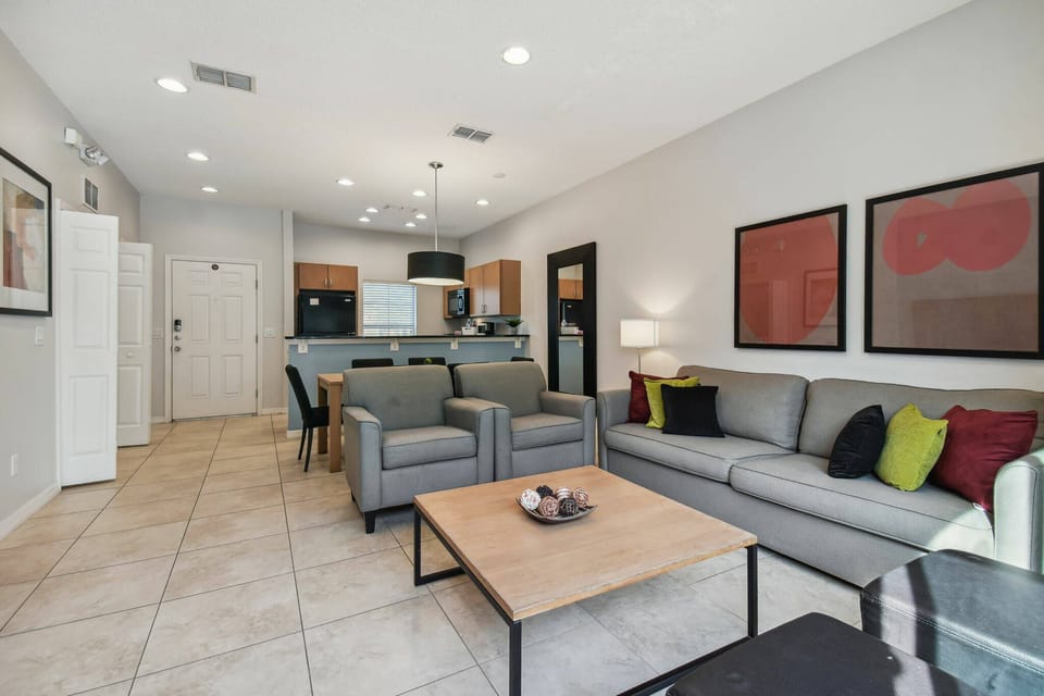 Bright and airy, this living room features plush gray sofas accented with vibrant pillows, creating a cozy atmosphere. The open layout seamlessly connects to a stylish kitchen, perfect for both relaxation and entertainment.