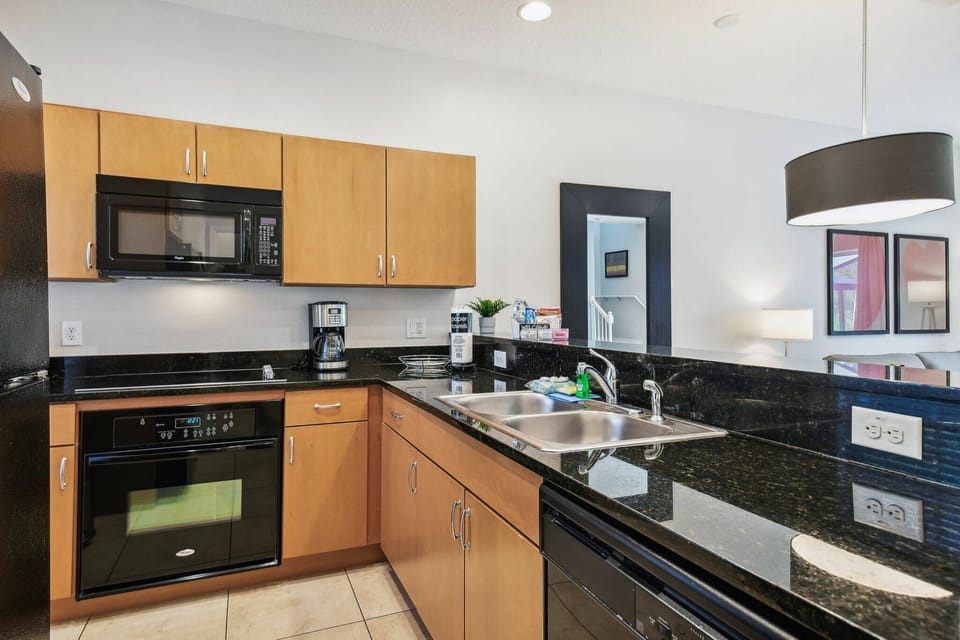 This stylish kitchen boasts sleek black granite countertops and warm wooden cabinetry, offering a functional cooking space. With modern appliances like a microwave and dishwasher, meal preparation becomes a breeze for guests.