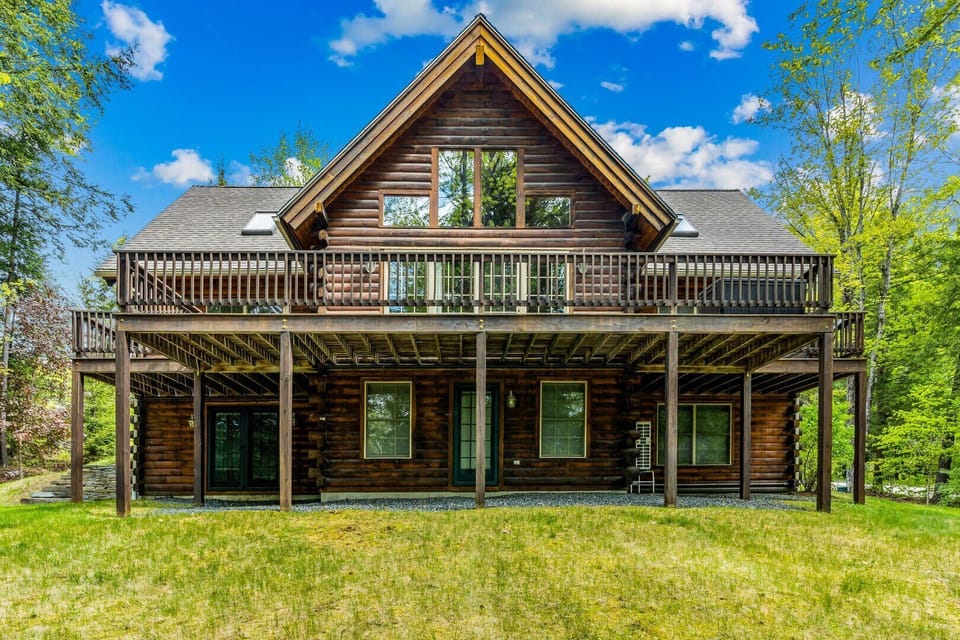 Full log cabin exterior with upper deck
    surrounded by Vermont woods — summer view