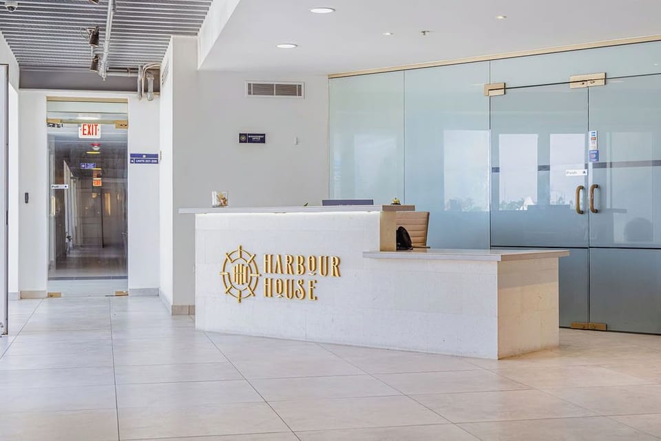 The modern reception area at Harbour House welcomes guests with sleek design, featuring a distinctive nautical logo and bright, airy atmosphere setting the tone for a coastal getaway.