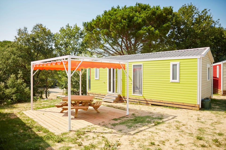 Charming mobil-home featuring a shaded deck with an orange awning and picnic table nestled among trees.