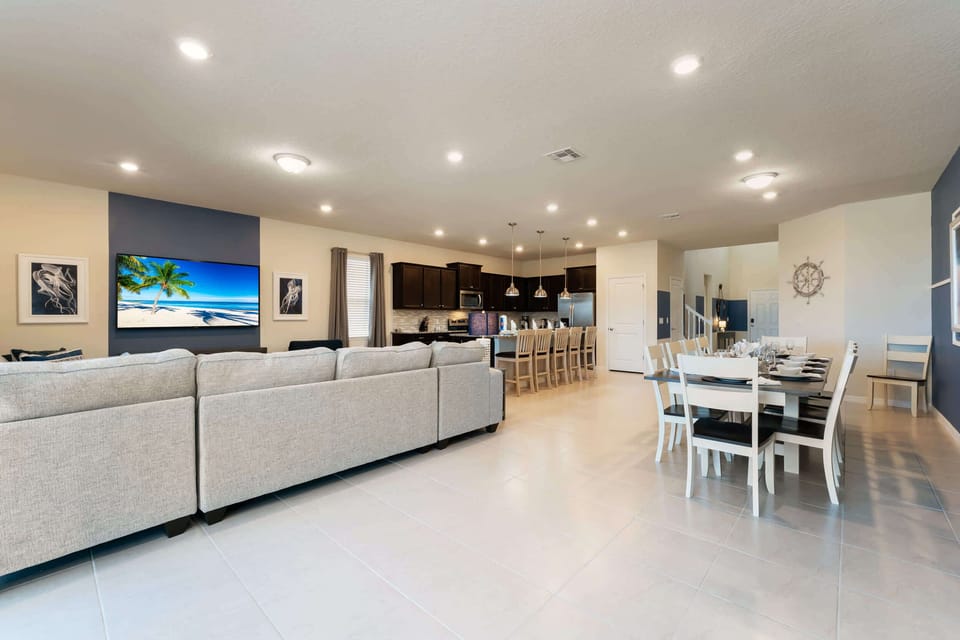 Spacious open-plan living area perfect for entertaining, featuring a large sectional, dining for 10, and a modern kitchen with bar seating.