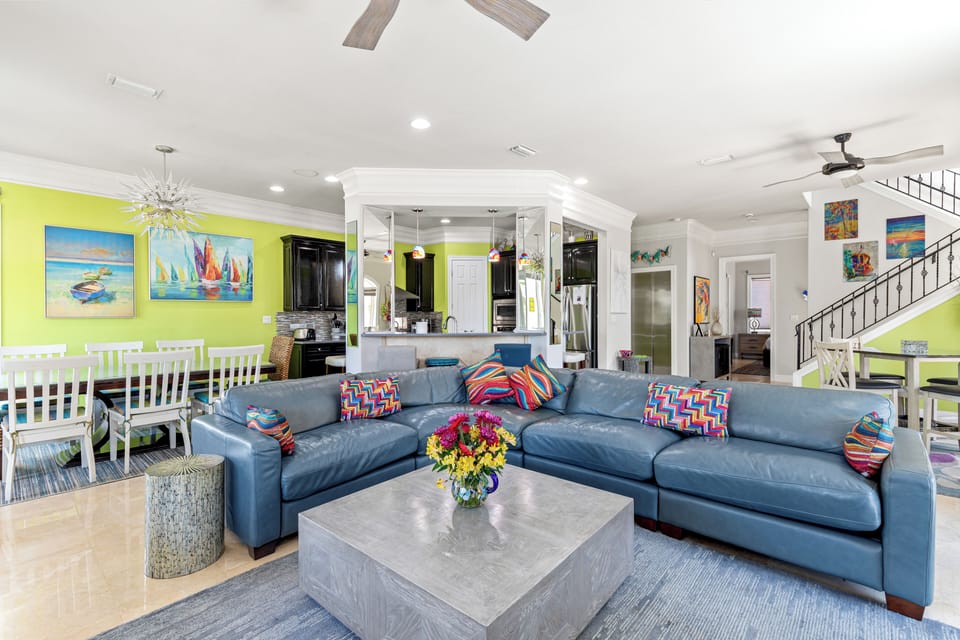 Relax in your vibrant living space with plush blue sectional seating, tropical artwork, and an open-concept layout perfect for gatherings.