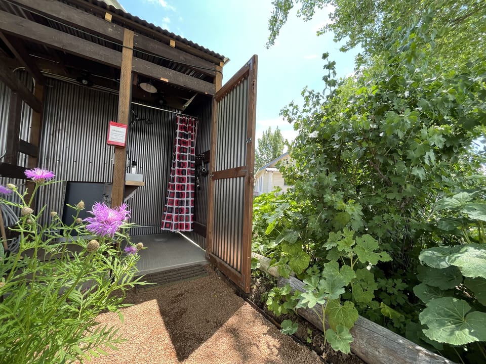 The outdoor shower has heated water and is located behind the small blue cottage