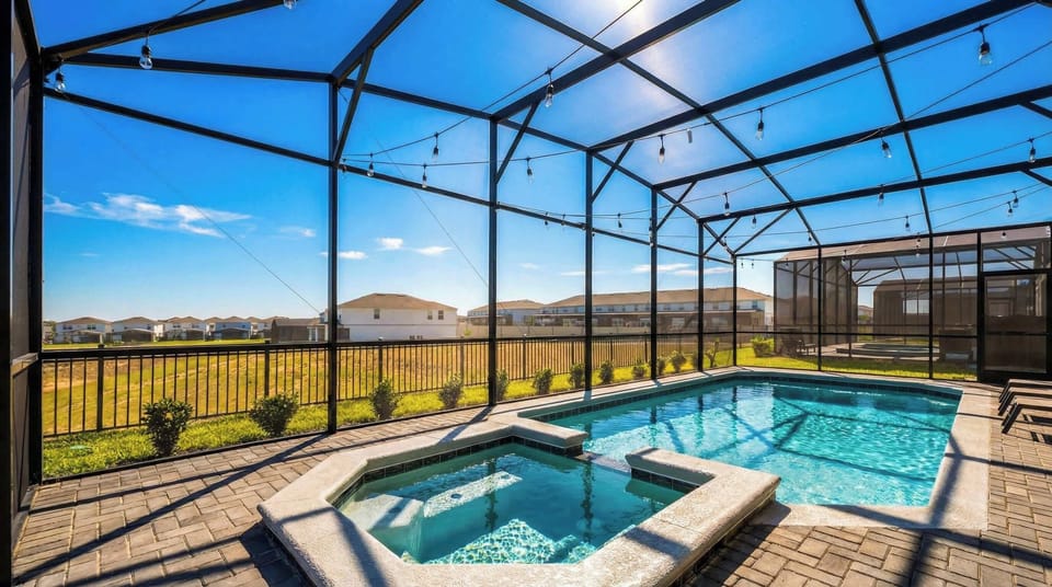 Sunny screened-in pool and spa with string lights, open views, and resort-style charm.