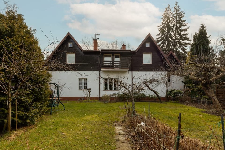 An exterior rear view of the house, surrounded by trees and a well-maintained garden.
