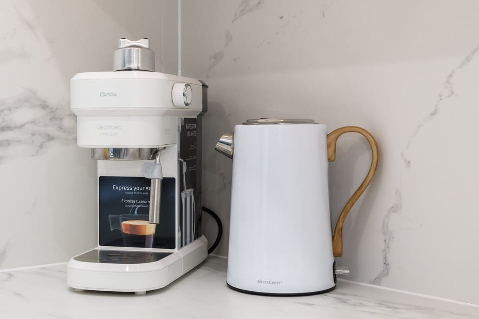 A coffee machine and white kettle on a marble countertop, combining functionality with style.
