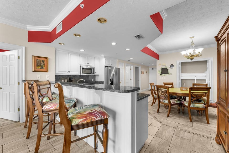 Open kitchen with granite countertops and seating that flows into a dining area with classic wooden chairs.