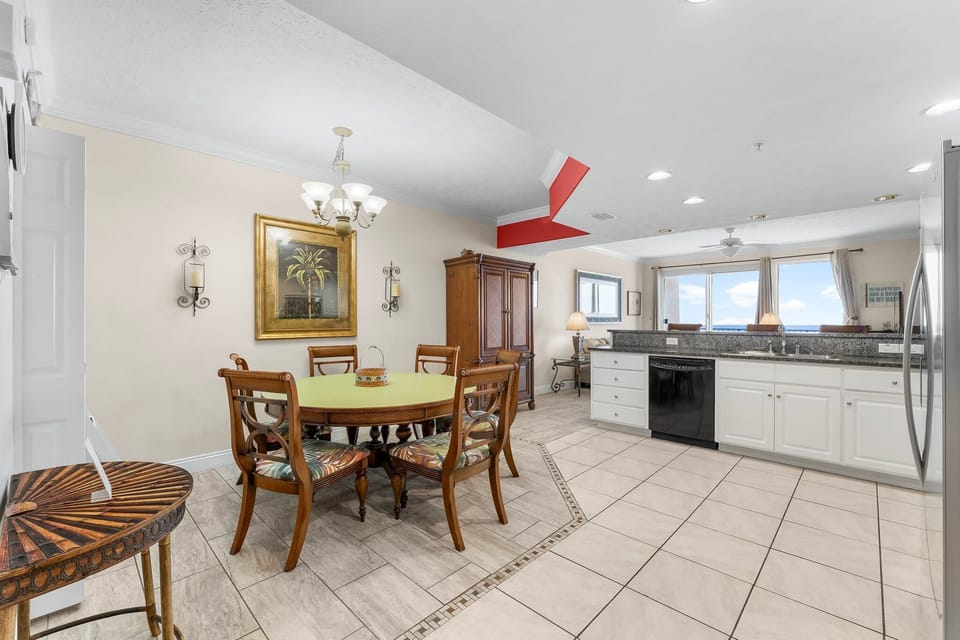 Dining area with classic wooden furniture adjacent to a bright kitchen featuring large windows.
