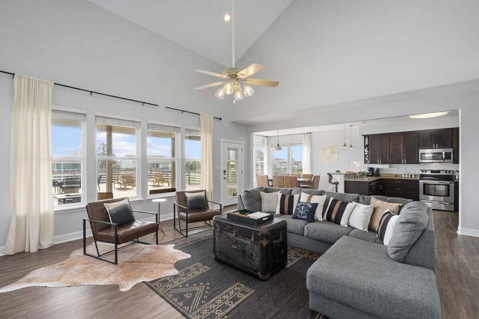 Comfortable living room with sectional sofa, accent chairs, fireplace, TV, ceiling fan, and open kitchen access.