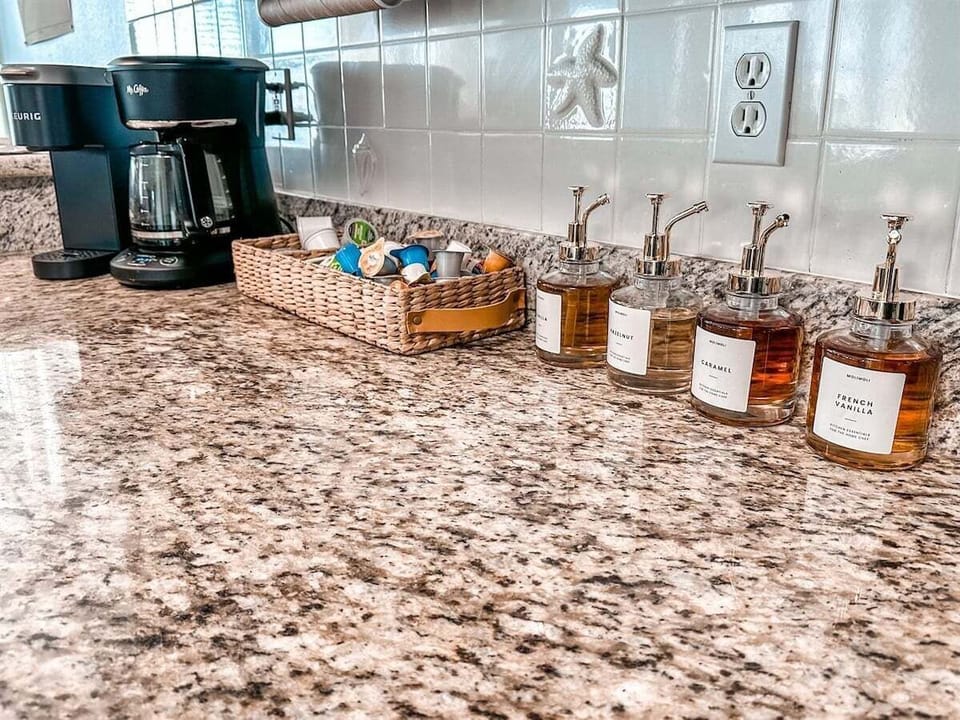 Kitchen coffee station with drip coffee maker, granite countertop, tile backsplash, and stocked beverage accessories.
