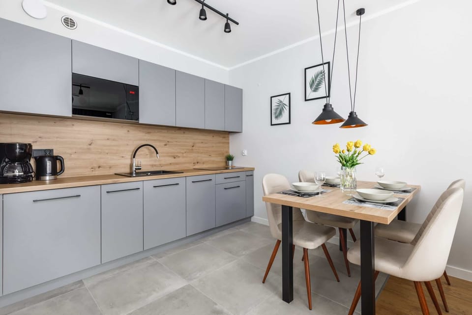 A small kitchenette with gray cabinets and wooden countertops. A dining table with chairs is adjacent, completing the compact layout.