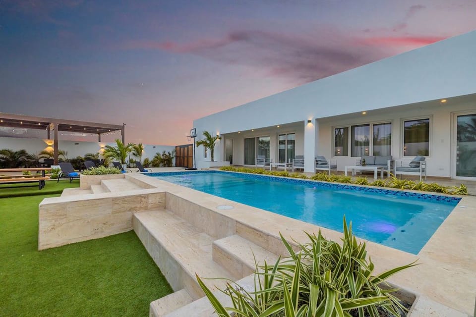 A modern vacation rental with sleek architecture, sparkling pool, and manicured grounds awaits beneath a pastel twilight sky—an elegant tropical retreat designed for relaxation.