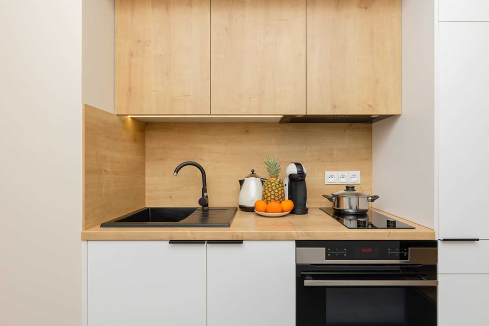 A compact kitchenette featuring white cabinets, wooden countertops, and essential appliances.
