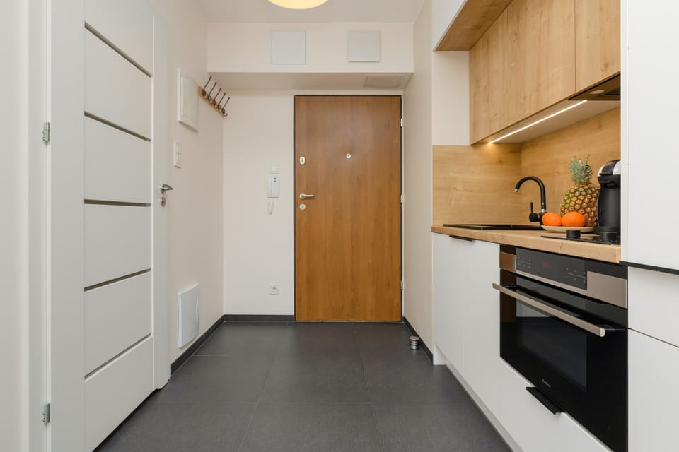 A modern kitchen with wooden cabinets, black countertops, and a sleek layout leading to the entrance.
