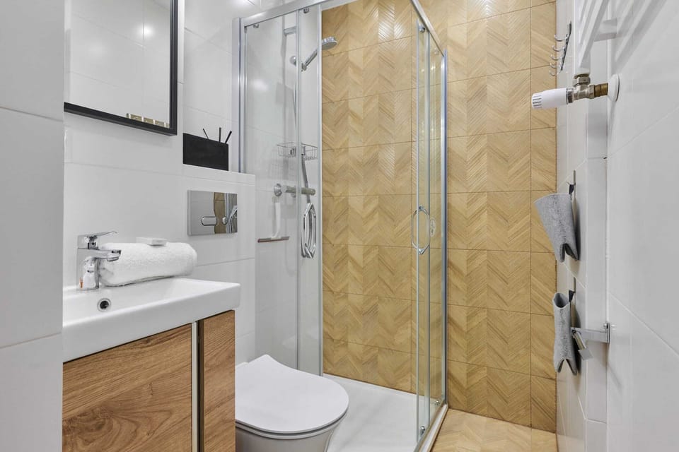 A bathroom with a glass shower, wooden vanity, and modern tile design.
