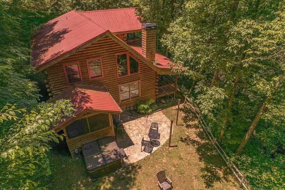 Elevated perspective showcasing the cabin, covered entry area, and outdoor patio seating nestled among mature trees near Bryson City.