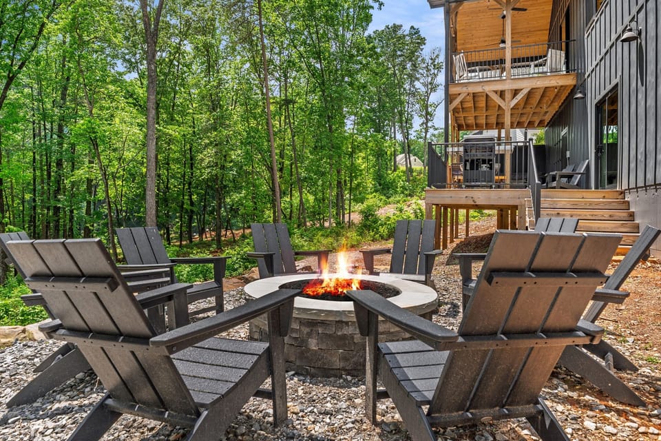 Outdoor gas fire pit with Adirondack seating at Yonah Mountain Farmhouse, surrounded by peaceful forest views. Enjoy cozy evenings near Helen, Georgia at this luxury cabin in the North Georgia Mountains, perfect for gathering and relaxing.