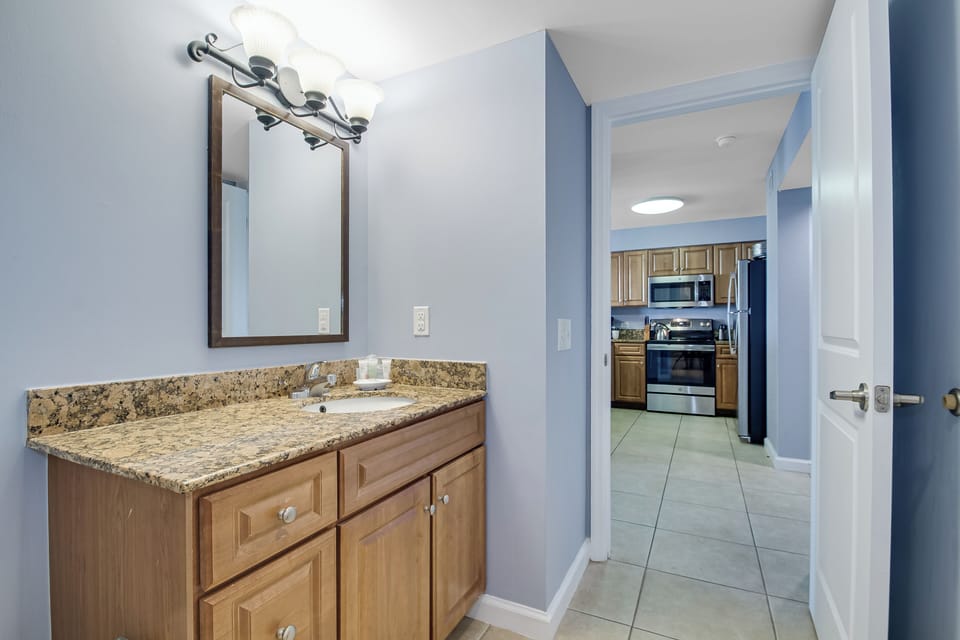 Your private bathroom vanity gleams with granite countertops and warm wood cabinetry, perfectly positioned near your fully equipped kitchen.