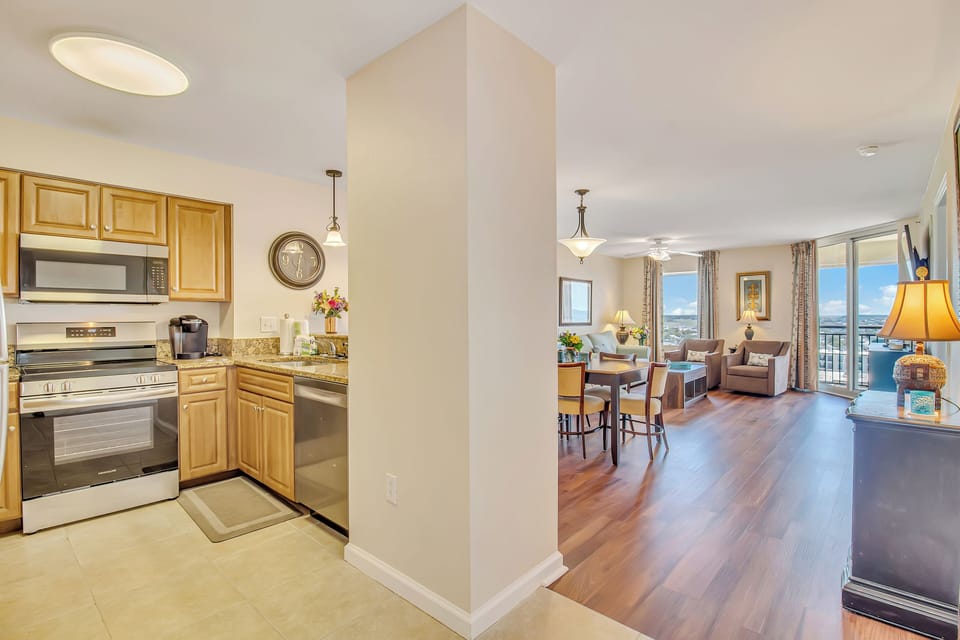 Your open-concept space flows seamlessly from kitchen to living area, featuring warm wood tones and stunning city views through floor-to-ceiling windows.
