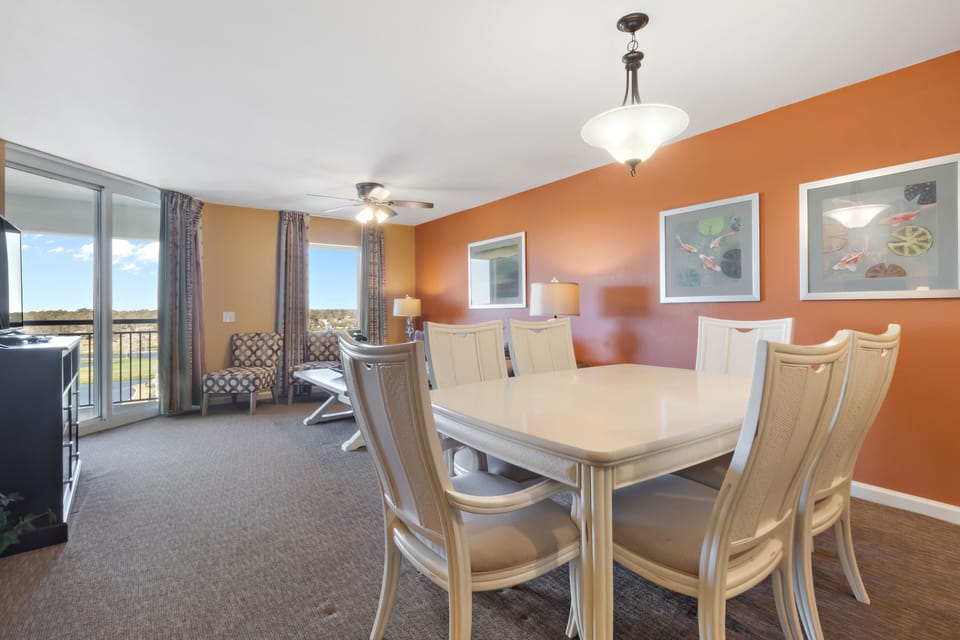 Gather around your spacious dining table for memorable meals with warm orange walls and natural light streaming through your private balcony doors.