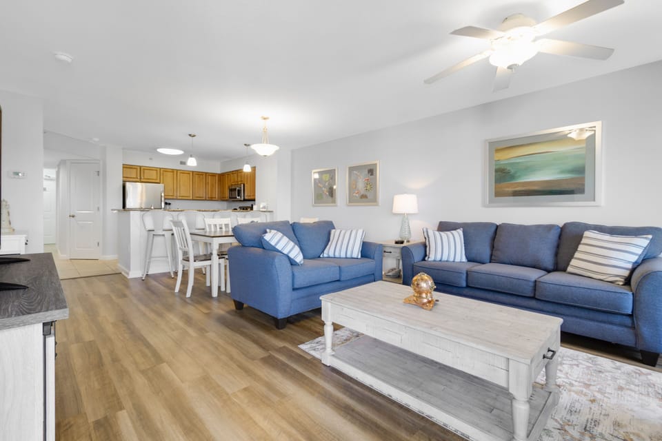 Relax in your spacious open-plan living area with comfortable blue sofas, modern kitchen, and coastal-inspired decor creating the perfect beachside retreat.