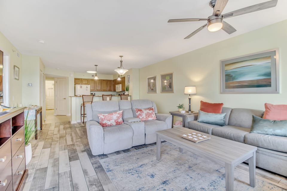 Unwind in your spacious open-concept living area with plush seating, ocean-inspired artwork, and gentle ceiling fan breeze creating perfect comfort.