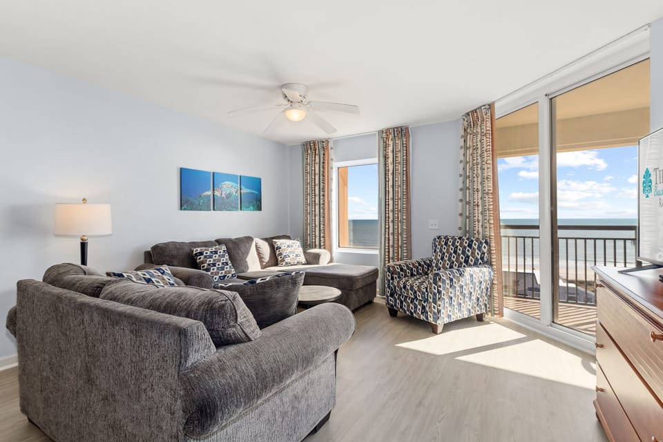 Relax in your spacious oceanfront living room with plush seating and panoramic sea views through floor-to-ceiling windows.