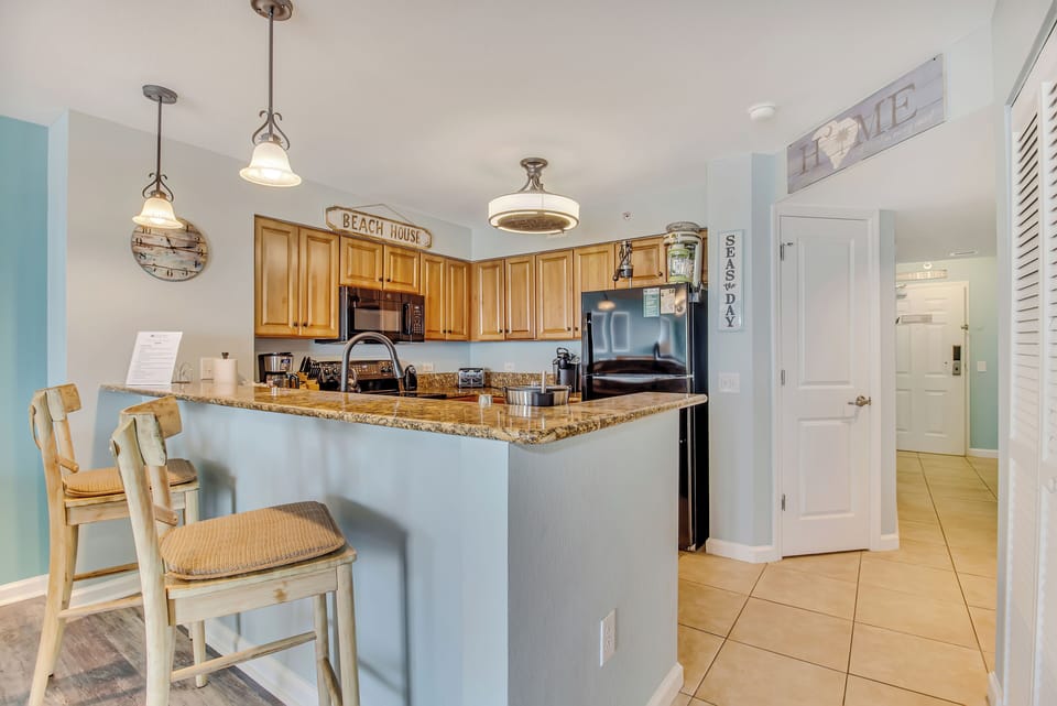 Your coastal kitchen awaits with warm wood cabinets, granite counters, and charming beach decor - perfect for morning coffee at the breakfast bar.