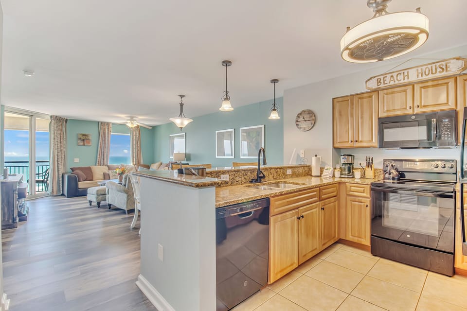 Your open-concept beachfront retreat features a fully-equipped kitchen flowing into the living area, where ocean views await through floor-to-ceiling windows.